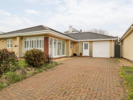A single-story house with a garage and driveway surrounded by plants at Haul a Gwynt in Trearddur Bay