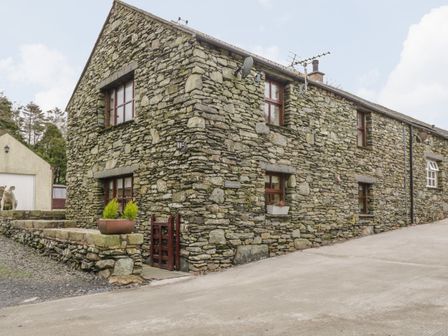 An exterior view of a stone cottage with multiple windows and a small garden area at Laithe Cottage in Pennington near Ulverston