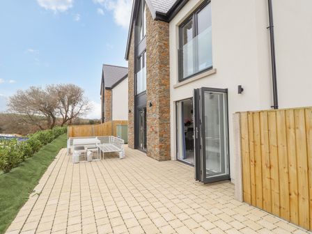 A paved patio area with outdoor seating next to a house with stone and white walls at Chandlers Retreat in Newport Pembrokeshire