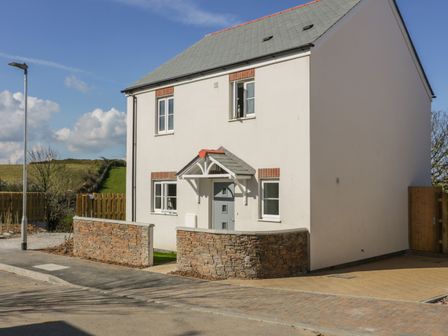 A two-story house with a gray door and four windows surrounded by a low stone wall at 4 Trerammet Crescent in Tintagel