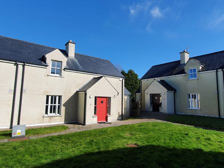 Two cream cottages with slate roofs and one red door and one brown door on a sunny day at 11 An Seanachai Holiday Homes in Ring County Waterford