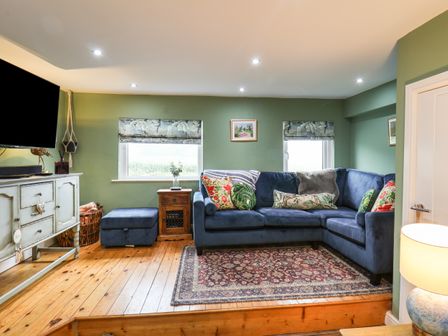 A living room with a blue sectional sofa wooden floors and green walls at The Seaside House in Staithes