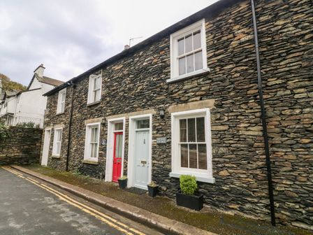 The exterior stone facade of a cottage with two front doors one red and one light blue on a street at Nutkin Cottage in Bowness-On-Windermere