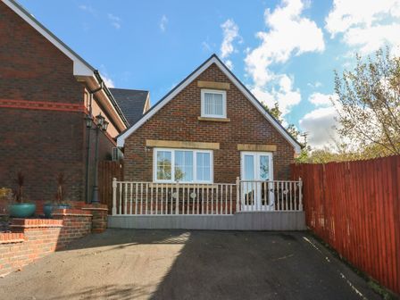 A brick house with white windows and a fenced front patio in a driveway at Ffau'r Ddraig in Cross Hands