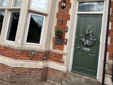 An exterior view of a house entrance with a green door and windows at Clairville, Hunstanton
