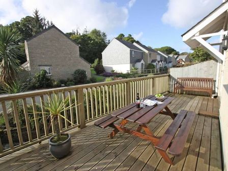 A wooden deck with a picnic table bench a potted plant and a bench overlooking houses and greenery at Waters Edge in Falmouth