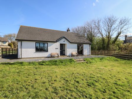 A white cottage with a grey roof two benches and a grass yard at Glyn Cottage in Llanon