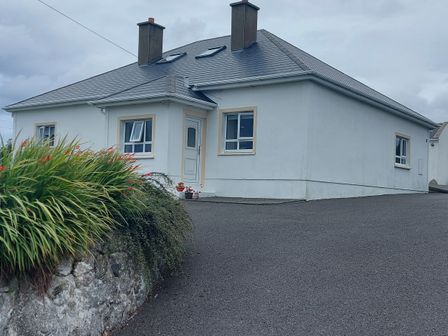 A white house with a grey roof and two chimneys with plants and a stone wall near the driveway at Ard an Phiobaire in An Luinnigh near Derrybeg County Donegal