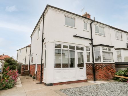 The exterior of a two story semi detached house with white walls and brick lower section at Sams Place in Whitby