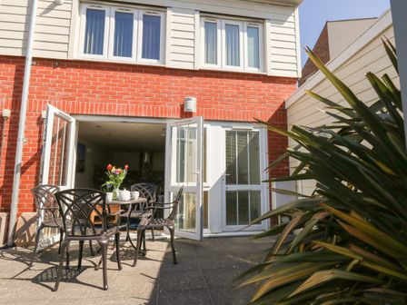 A patio with a table and chairs set outside a house with open glass doors and a large plant at Park Mews Weymouth