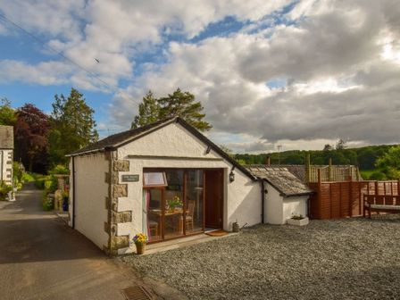 A white building with a wooden door and window next to a gravel area and road at Old Sawrey Stores Hawskhead