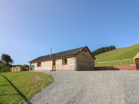 A wooden cabin with a gravel driveway and grass on a hillside at Ploony Hill Cabin in Bleddfa near Knighton