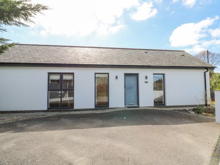 A single story house with a grey door and three tall windows on a paved driveway at Kensa in Carharrack near St Day