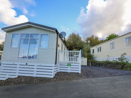 A mobile home with white siding and a small gated porch next to another similar mobile home at Ystwyth 26 in Borth