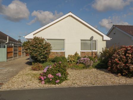 A single story house with two windows and a gravel front garden with bushes and flowers at Seaside retreat in Porthmadog