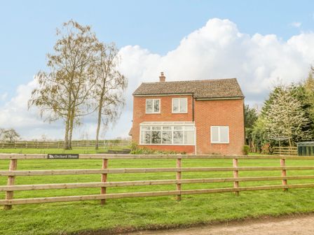 A brick house with multiple windows behind a wooden fence and trees at Orchard House in Risbury near Leominster