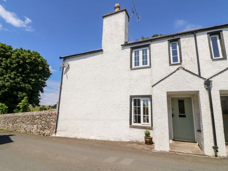 An exterior view of a white two-story house with a stone wall and tree nearby at St Peters Cottage in Milnthorpe