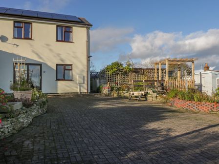 A paved driveway next to a two-story house with a garden and wooden trellis at The Annex in Drybrook