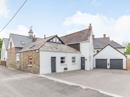 A building with mixed stone and white walls with two dark gray doors and a double garage at The Old Coach House in Braunton