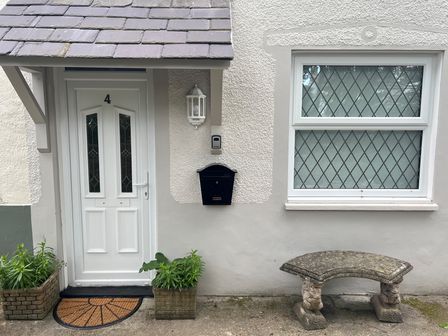 A white front door with number 4 a black mailbox two plant pots and a stone bench with a window at 4 Railway Terrace in Conwy