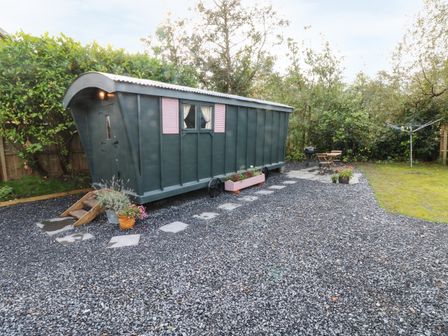 A garden area with a small green caravan a gravel path and outdoor seating at Hazel Nook in Narberth