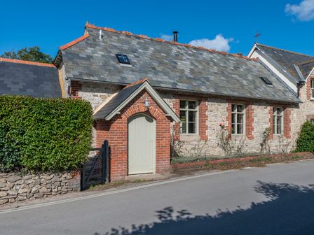 A stone and brick house with a slate roof and arched doorway by a hedge at St Mary's Chapel in West Lulworth