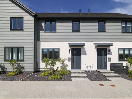 The exterior of a modern semi detached house with two grey front doors and windows with a small garden area at Dune Retreat in Llanfaelog near Rhosneigr