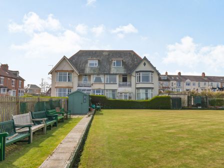 A lawn with benches and a shed in front of a large residential building at Beachside Apartment in Hornsea