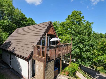 A two-story house with a sloped roof and wooden balcony surrounded by trees at 59 Valley Lodge Callington near Gunnislake