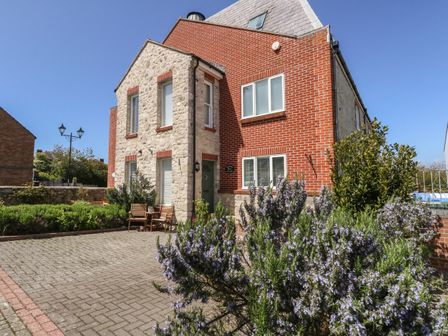 A two-story house with stone and brick exterior a paved driveway and flowering bushes at The Brewery in Brewers Quay Harbour