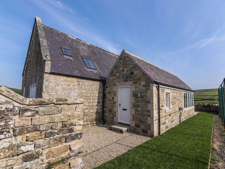 A stone building with a pitched roof a white door and green grass surrounding it at Greystead Institute in Bellingham