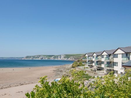 A beach with a few people on the sand and a row of buildings with balconies on the right side at 17 Burgh Island Causeway in Bigbury-On-Sea