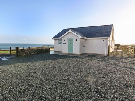 A single-story house with a green front door and gravel driveway with sea view at Y Gorlan in Moelfre