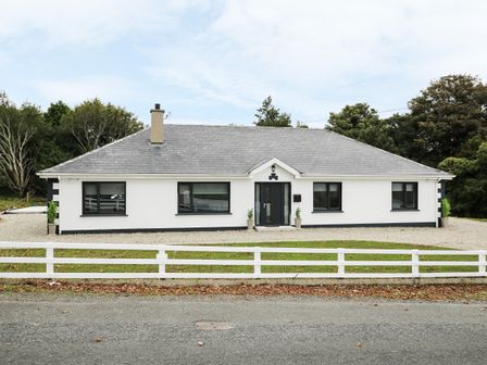 A single story white house with gray roof and black framed windows behind a white fence at Gatehouse in Moville County Donegal