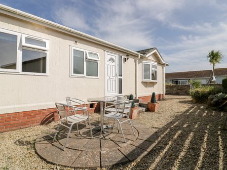 An outdoor seating area with a round table and four metal chairs outside a beige house at Summer Breeze in Tregolds near St Merryn
