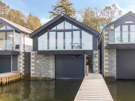 A boathouse with glass balcony and patio furniture by the water at Boathouse on the Lake in Bowness-On-Windermere