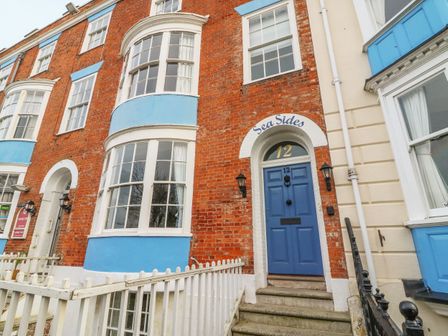 The exterior entrance of a red brick building with blue door and blue trim around windows at Seasides in Weymouth