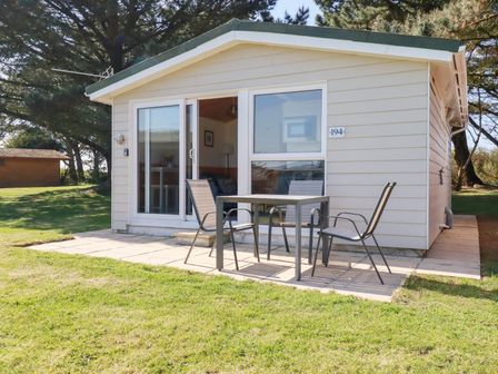 A small house with a patio table and three chairs on a paved area at 194 Atlantic Bays Holiday Park near St Merryn