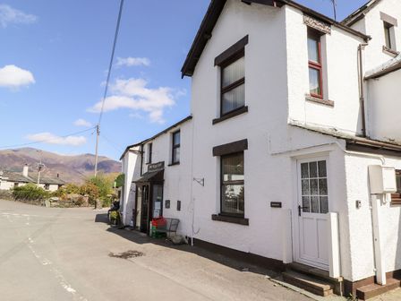 A white building with a shop entrance and a white door on a street with mountains in the background at Holme Rigg in Braithwaite