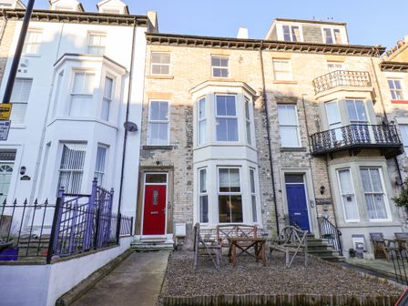 A row of terraced houses with a red door and outdoor wooden furniture on a gravel front yard at 4 Normanby Terrace Whitby