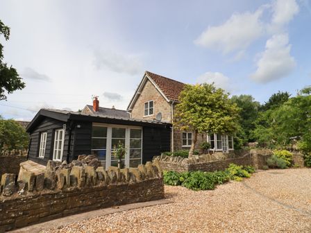 A stone house with a black wooden extension surrounded by a stone wall and plants at The Coach House in Ross-On-Wye