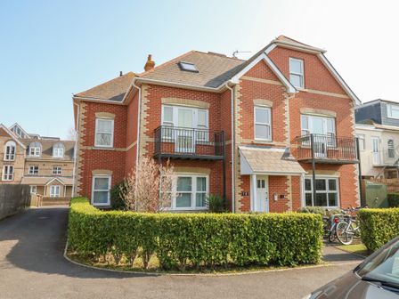 A brick two-story house with balconies and a hedge in front at Harbour Reach 6 in Weymouth