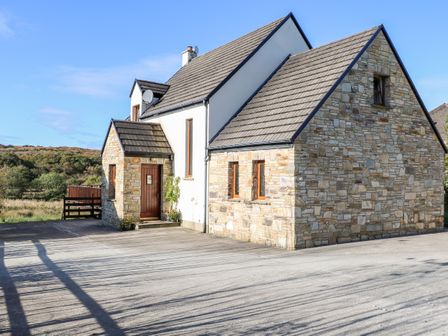 A stone house with a tiled roof and wooden door on a concrete driveway at Crolly Home in Crolly County Donegal
