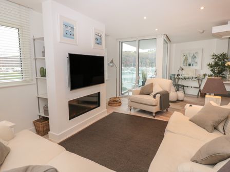 A living room with sofas a wall-mounted TV fireplace and a view of boats through glass doors at 2 Sails in Dartmouth