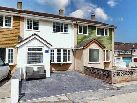 A row of houses with a paved driveway and bench outside at Beach Cottage in Portreath