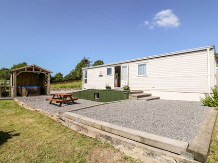 An exterior view of a mobile home with gravel patio area wooden picnic table and covered hot tub at The Lodge in Pontyates