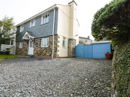 A two-story house with a stone and slate exterior next to a gravel driveway and blue wooden fence at Hazel Cottage in Tintagel