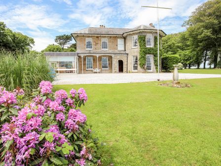 A stone house with a lawn and pink flowers in front at Tal Gwynedd in Dwyran near Newborough