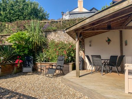 An outdoor seating area with black chairs under a wooden pergola and additional black chairs with a small table on a gravel surface at Simples in Dartmouth