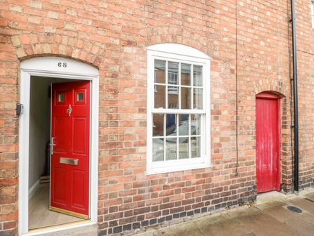 A red door open next to a window and a smaller red door on a brick building at Heath Cottage in Stratford-Upon-Avon